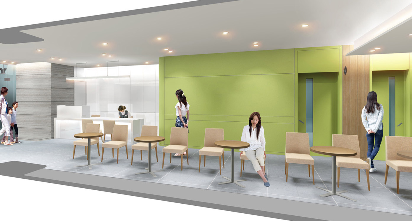 新教室の待機スペース。壁際に受付カウンター、小テーブルと椅子が並ぶ。壁面の色はイエローグリーン